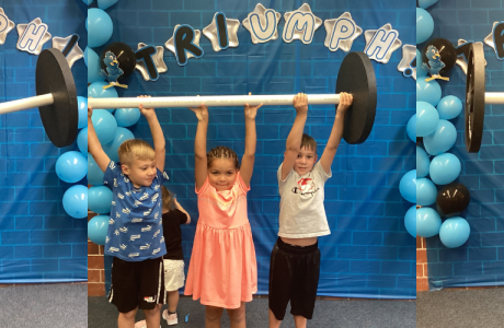 Students holding up weight bar in front of triumph sign